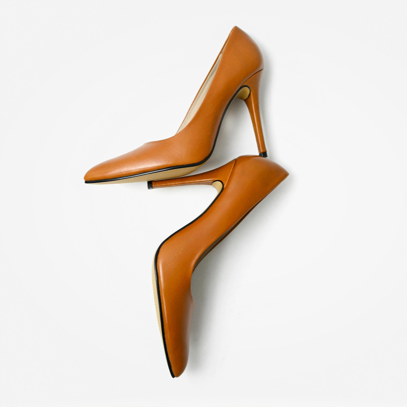 Pair of matte tan leather high heels arranged diagonally on a clean white surface.
